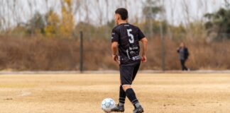 A soccer player in black jersey prepares to pass on an outdoor field.