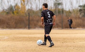 A soccer player in black jersey prepares to pass on an outdoor field.