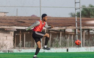 Young male soccer player practicing on outdoor field with red jersey.