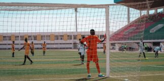 Soccer players in action during a competitive match, focusing on the goalkeeper's stance.