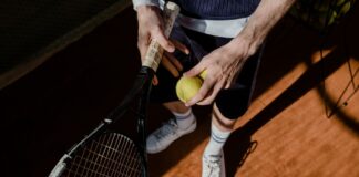 A tennis player prepares for a serve, holding a racket and tennis ball on a clay court.