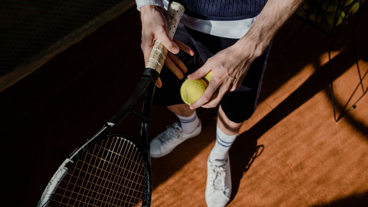 A tennis player prepares for a serve, holding a racket and tennis ball on a clay court. A tennis player prepares for a serve, holding a racket and tennis ball on a clay court.
