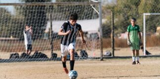 Teen soccer player dribbling the ball during a match on a sunny day outdoors.