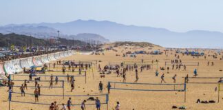 Aerial view of multiple beach volleyball games on a sunny day at a busy coastal beach.