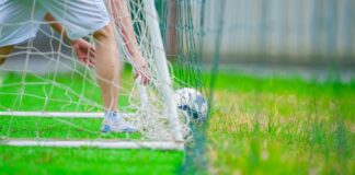 A soccer player retrieves a ball from the goal on a lush green field, captured in Hanoi, Vietnam.