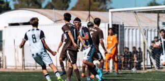 Intense soccer match with players challenging near the goal on a sunny day.