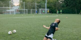 Female soccer player celebrating with arms raised on outdoor field.