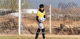 A young soccer goalkeeper standing on the field, holding a ball during the day.