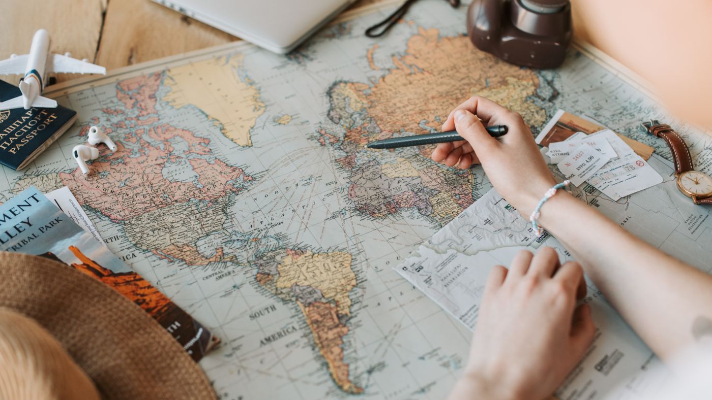Mani che segnano destinazioni su una mappa con passaporto e fotocamera