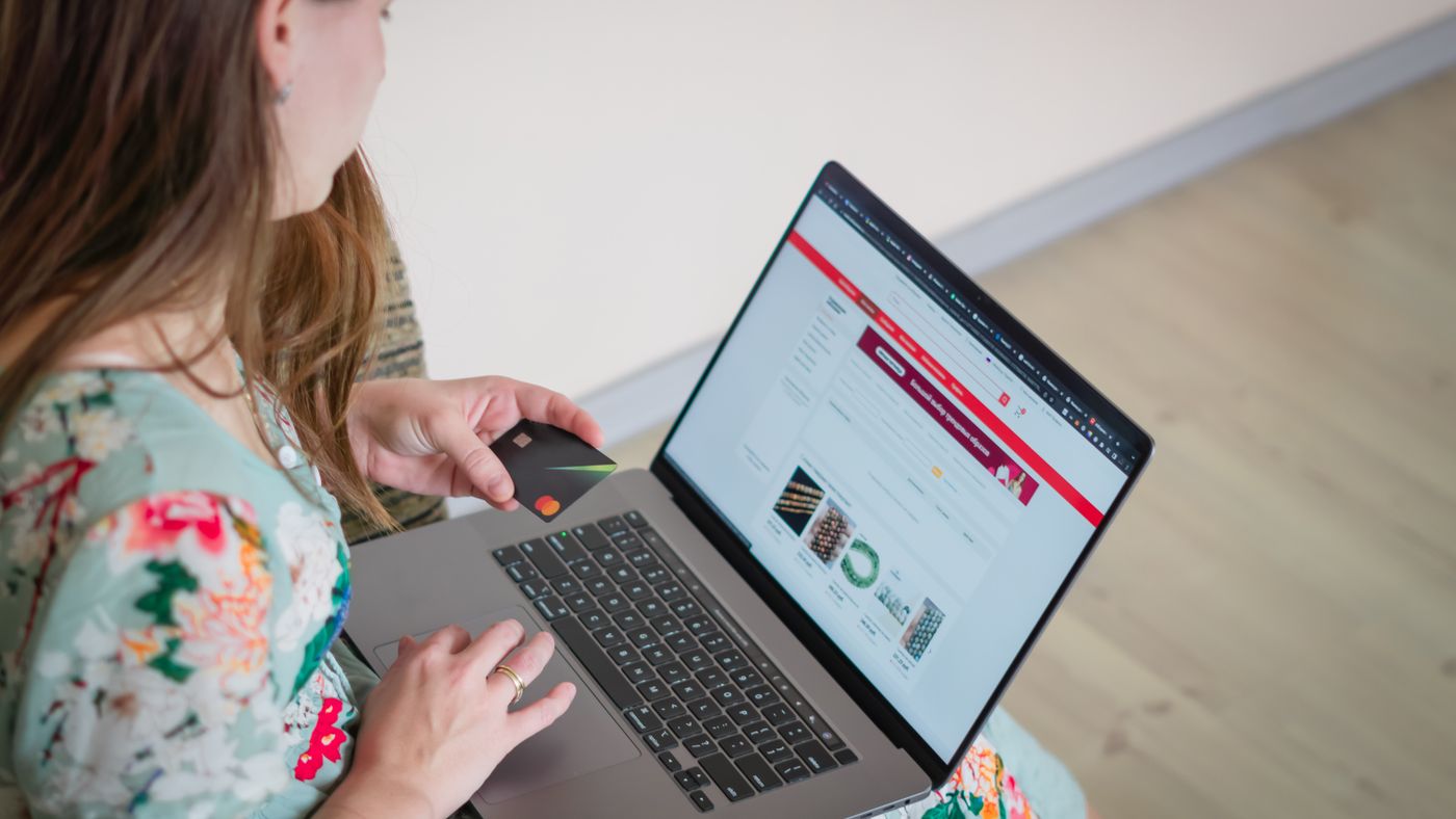 Donna in abito floreale fa shopping online con laptop e carta