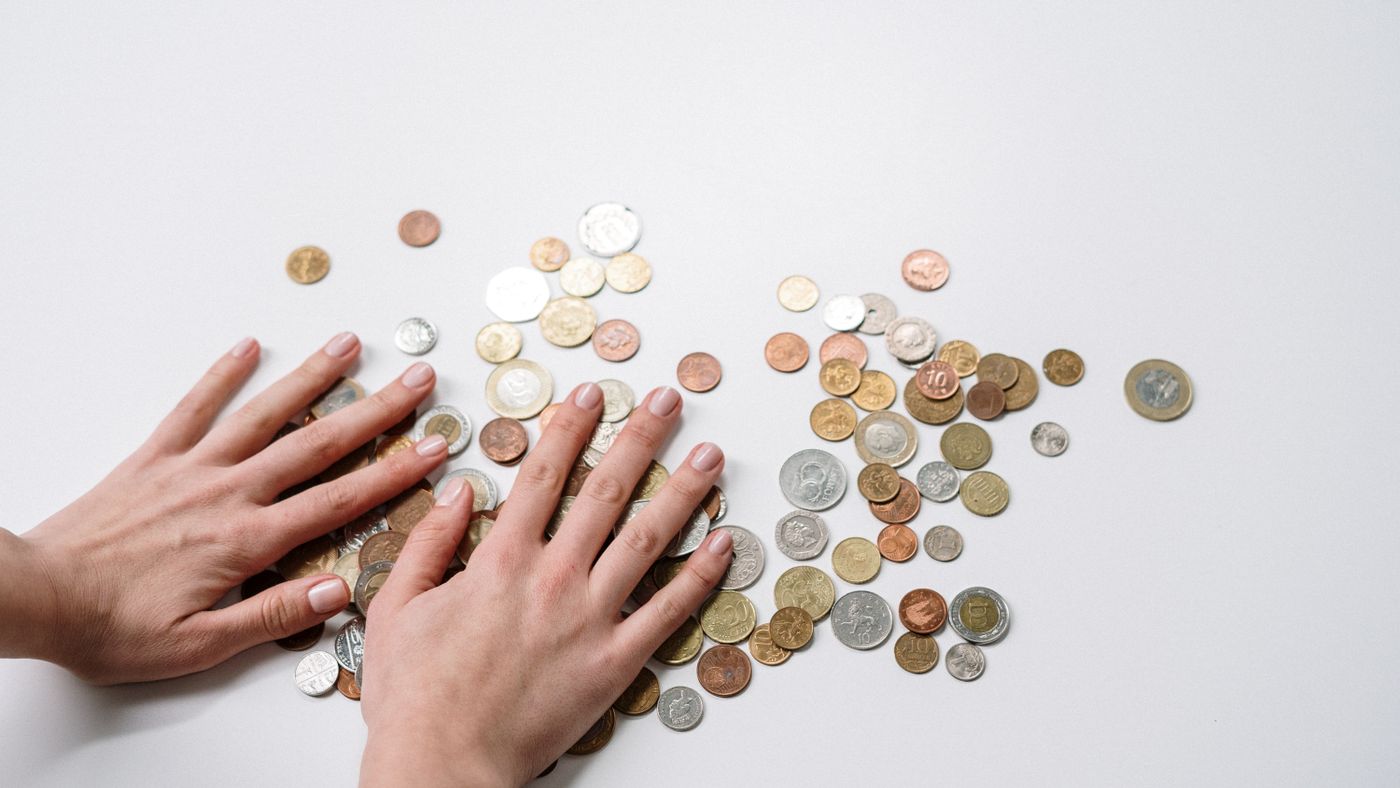 Mani che dispongono monete internazionali su sfondo neutro