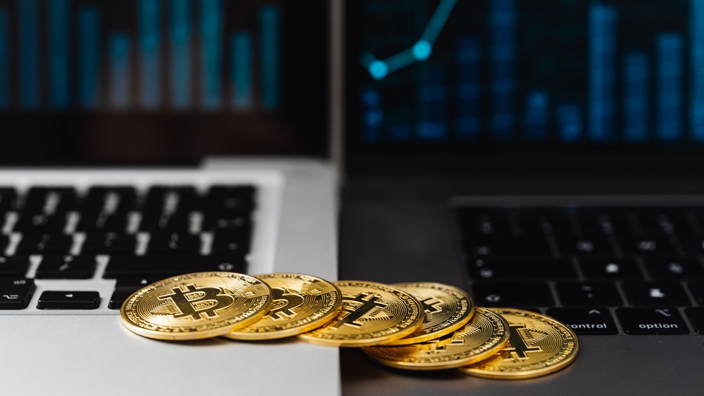 Bitcoin dorati su tastiere di laptop con grafici finanziari sullo sfondo